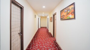 A hotel hallway with patterned carpet, wooden doors, and framed artwork on the walls. - Saver Single Royal Inn (New Delhi)