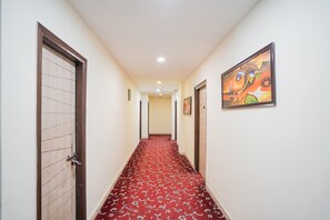 A hallway with patterned carpet, wooden doors, and a framed painting on the wall. - Saver Single Royal Inn (New Delhi)