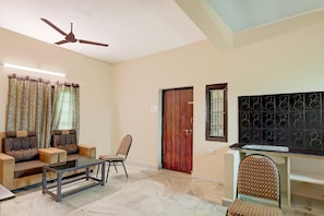 A living room with a sofa, chairs, a coffee table, a ceiling fan, and a TV.