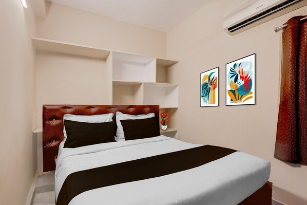 A hotel room with a bed, a headboard, a wall-mounted air conditioner, and two framed artworks.