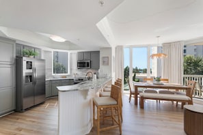 A modern kitchen with a central island, grey cabinetry, stainless steel appliances, and a dining area with wooden furniture and a view of the outdoors. - Spacious 3 bed 3 bath @ Silver Shells in Destin - Sleeps 8 (Destin)