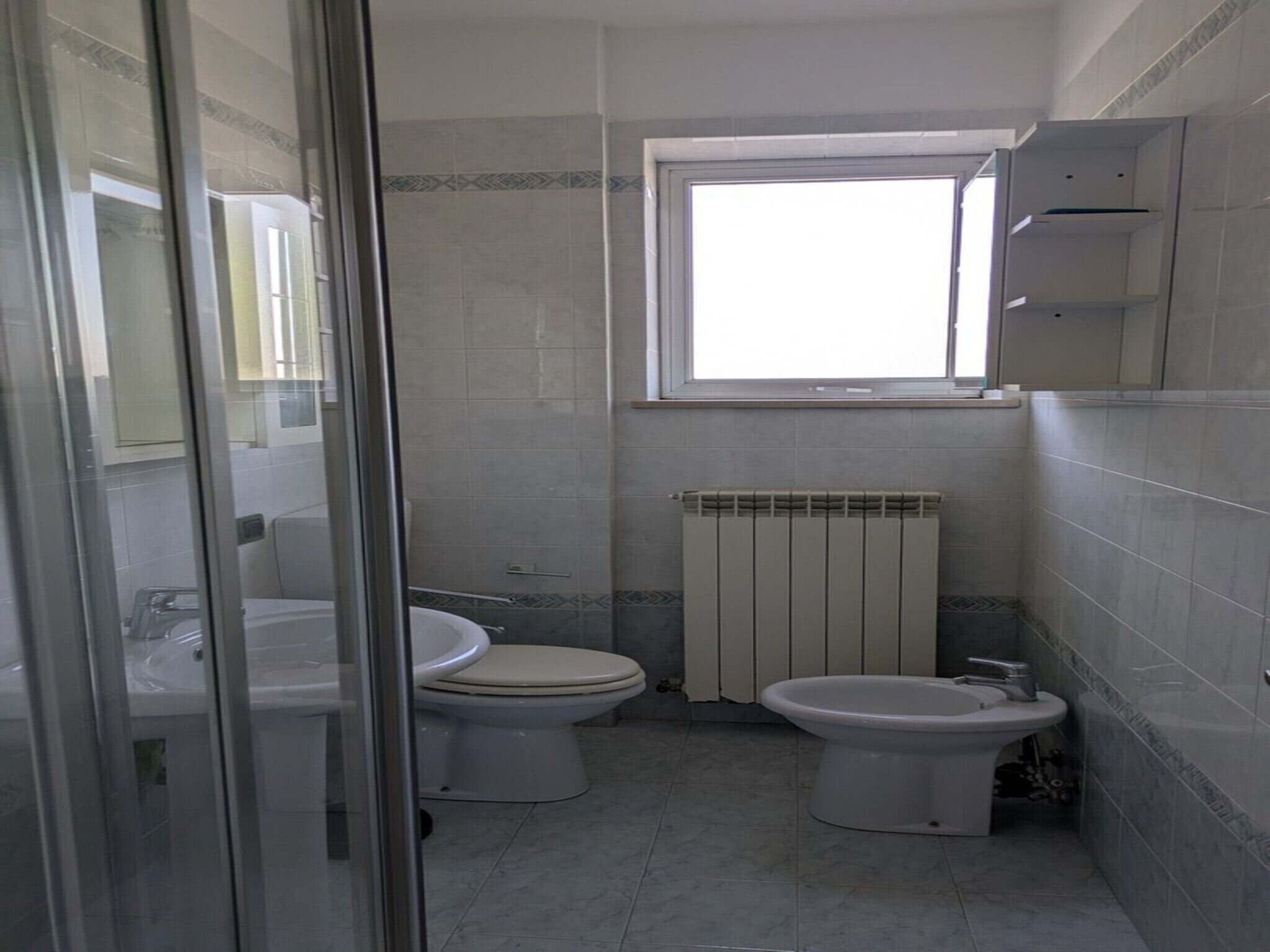 Egy fürdőszoba két WC-vel, bidével, ablakkal és radiátorral.