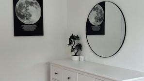 Ein Zimmer mit einem weißen Schminktisch, einer Bonsai-Pflanze und zwei gerahmten Bildern von Himmelskörpern an der Wand.