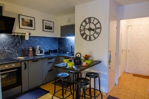 A compact kitchen with a built-in oven, a microwave, and a coffee maker. There are two stools at a small table with cups and a kettle. - Beautiful apartment with pool close to the beaches (Sainte-Maxime)