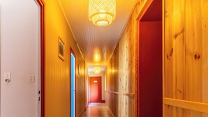Um corredor de madeira com luminária no teto, paredes de madeira e uma porta vermelha no final.