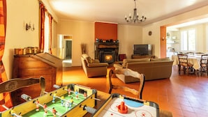 Uma sala de estar com mesa de pebolim, lareira, televisão e área de jantar.