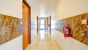 A hallway with marble walls, a fire extinguisher mounted on the wall, and a door labeled '106'. - Classic With Twin Bed Kaveri Road Mysore (Mysore)