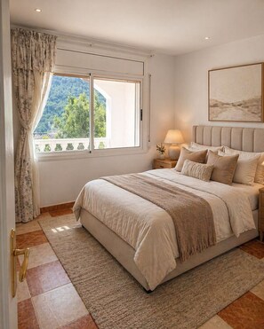 Ein Schlafzimmer mit einem großen Bett, einem Nachttisch, einer Lampe, einem Fenster mit Vorhängen und einem Bild an der Wand.