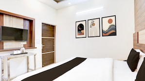 Ein Hotelzimmer mit Bett, Fernseher, einem kleinen Tisch mit Tassen und Wasserkocher sowie drei gerahmten Kunstwerken an der Wand.
