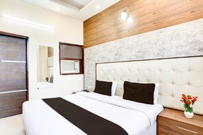 A modern hotel room with a large bed, a wooden accent wall, a marble headboard, and a nightstand with a vase of flowers. - Saver Double Hotel Prabhat (Dera Bassi)