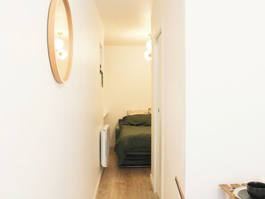 A narrow hallway with a radiator, a bed with green bedding, and a mirror on the left wall. - Studio near Roland Garros and Parc des Princes (Boulogne-Billancourt)