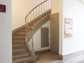 A staircase with wooden steps and metal railings, a door with a bulletin board, and a red object on the wall. - Studio near Roland Garros and Parc des Princes (Boulogne-Billancourt)