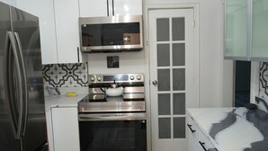Eine kompakte Küche mit Edelstahl-Kühlschrank, Backofen, Mikrowelle und einer Wanduhr.