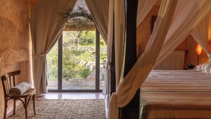 Una habitación con cama, un banco, una ventana con cortinas y vistas al exterior.