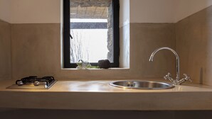 Una cocina con estufa a gas, pileta de acero inoxidable y ventana con vista a árboles.