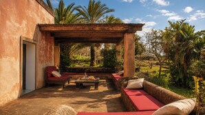 Un espacio exterior con paredes de piedra, una pérgola de madera y un sofá rojo acolchado.