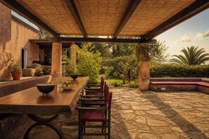 Une terrasse extérieure avec une longue table en bois, des chaises et un sol en pierre.