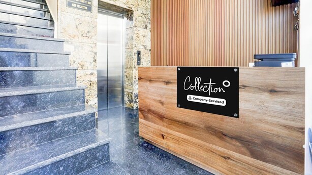 A reception desk with a sign reading 'Collection,' a stone wall, a wooden panel wall, and a clock. - Deluxe City Center Ludhiana MMC Inn (Ludhiana)