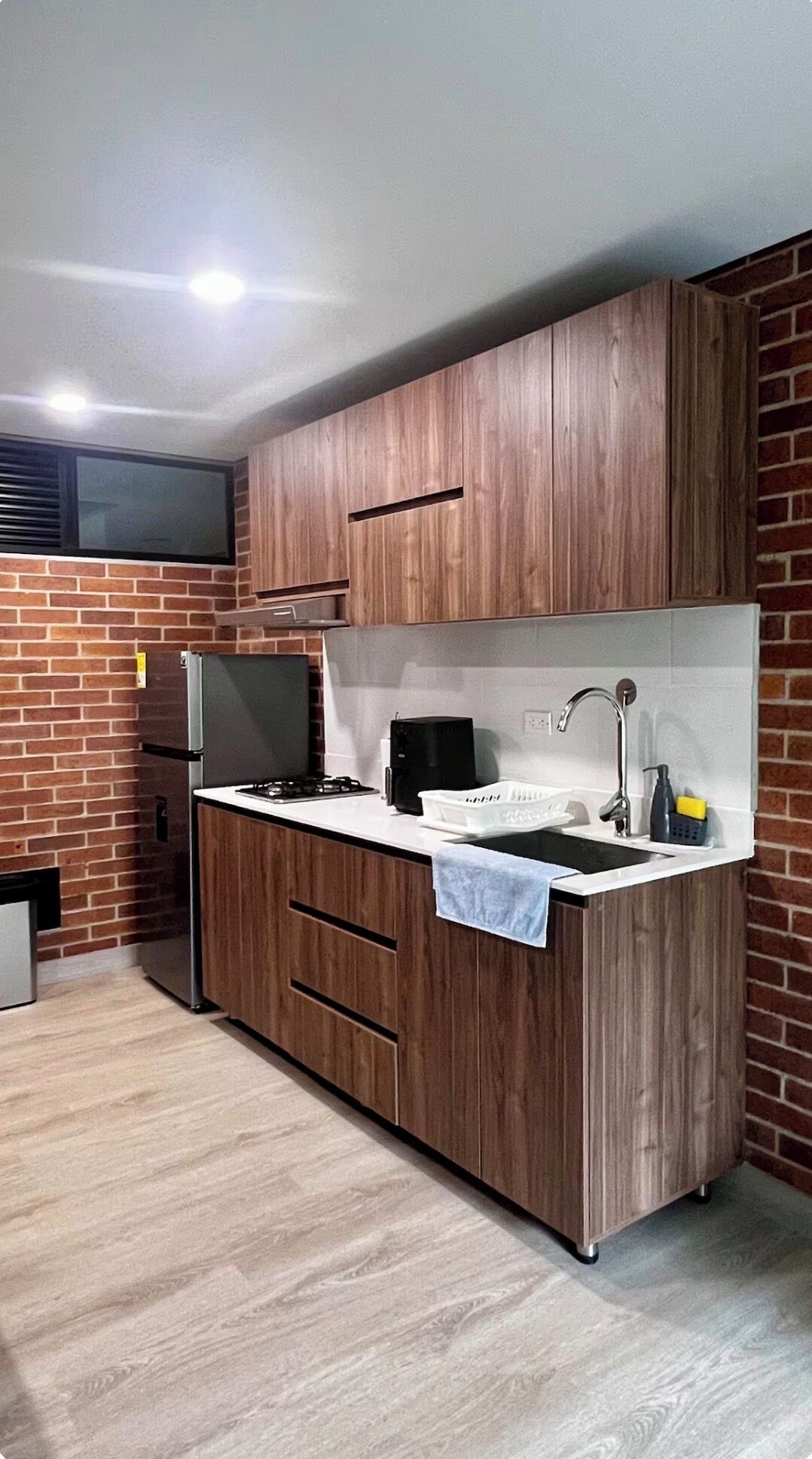 Una cocina compacta con armarios de madera, un lavamanos integrado y una estufa a gas.
