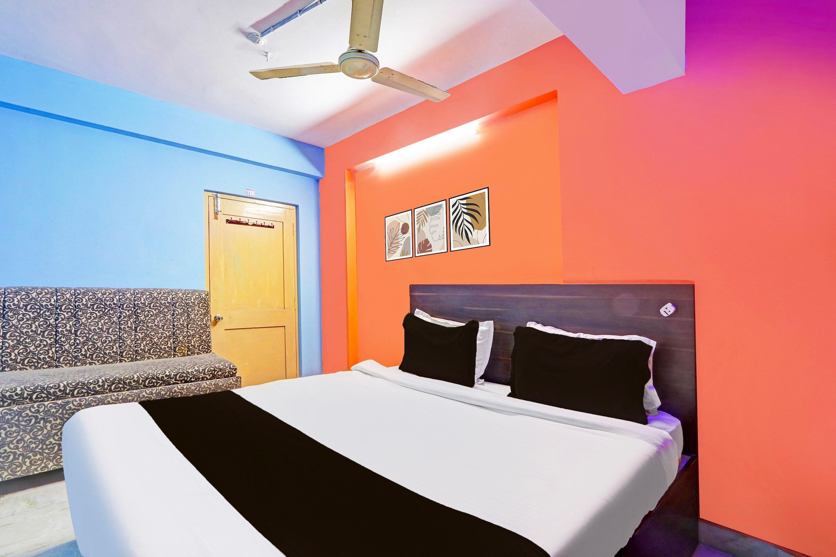 A room with a bed, a ceiling fan, a door, and a wall with framed pictures.