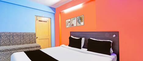 A room with a bed, a ceiling fan, a door, and a wall with framed pictures.