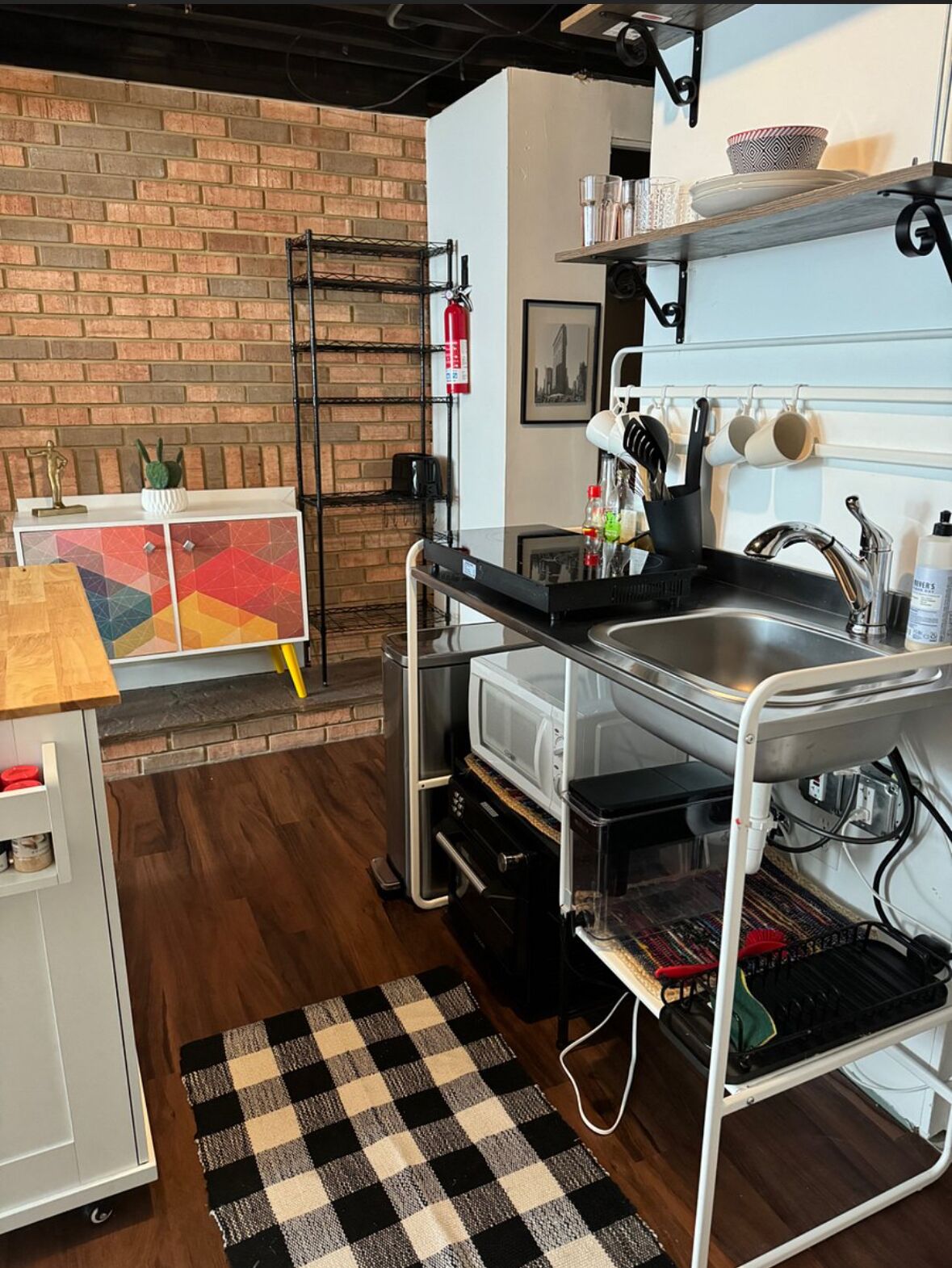 A compact kitchen with a brick wall, a microwave, a sink, and a small countertop.