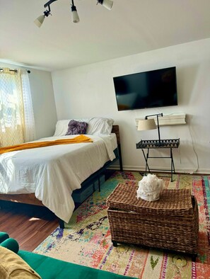 A bedroom with a bed, a TV, a lamp, a small table, and a colorful rug.