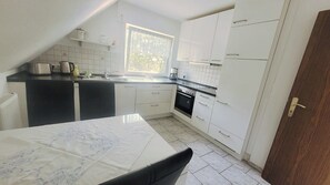 A kitchen with white cabinets, a black countertop, a window, and a door. - Vacation apartment "Langeoog" (Hage)