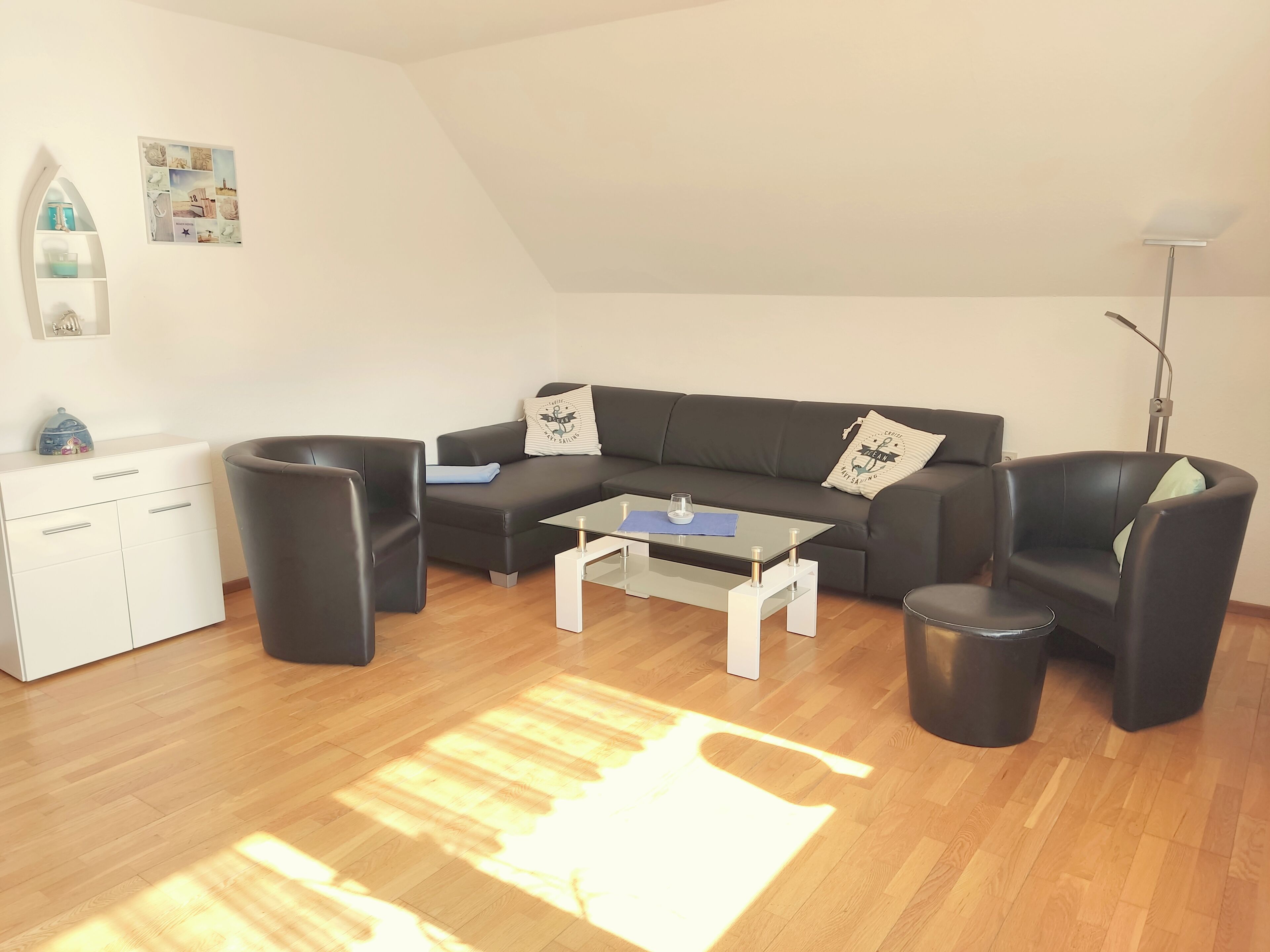 Ein modernes Wohnzimmer mit einer schwarzen Couch, einem Glastisch, einem weißen Schrank und einer Stehlampe.
