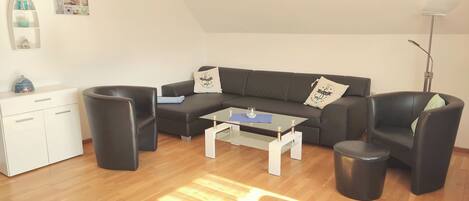 Ein modernes Wohnzimmer mit einer schwarzen Couch, einem Glastisch, einem weißen Schrank und einer Stehlampe.