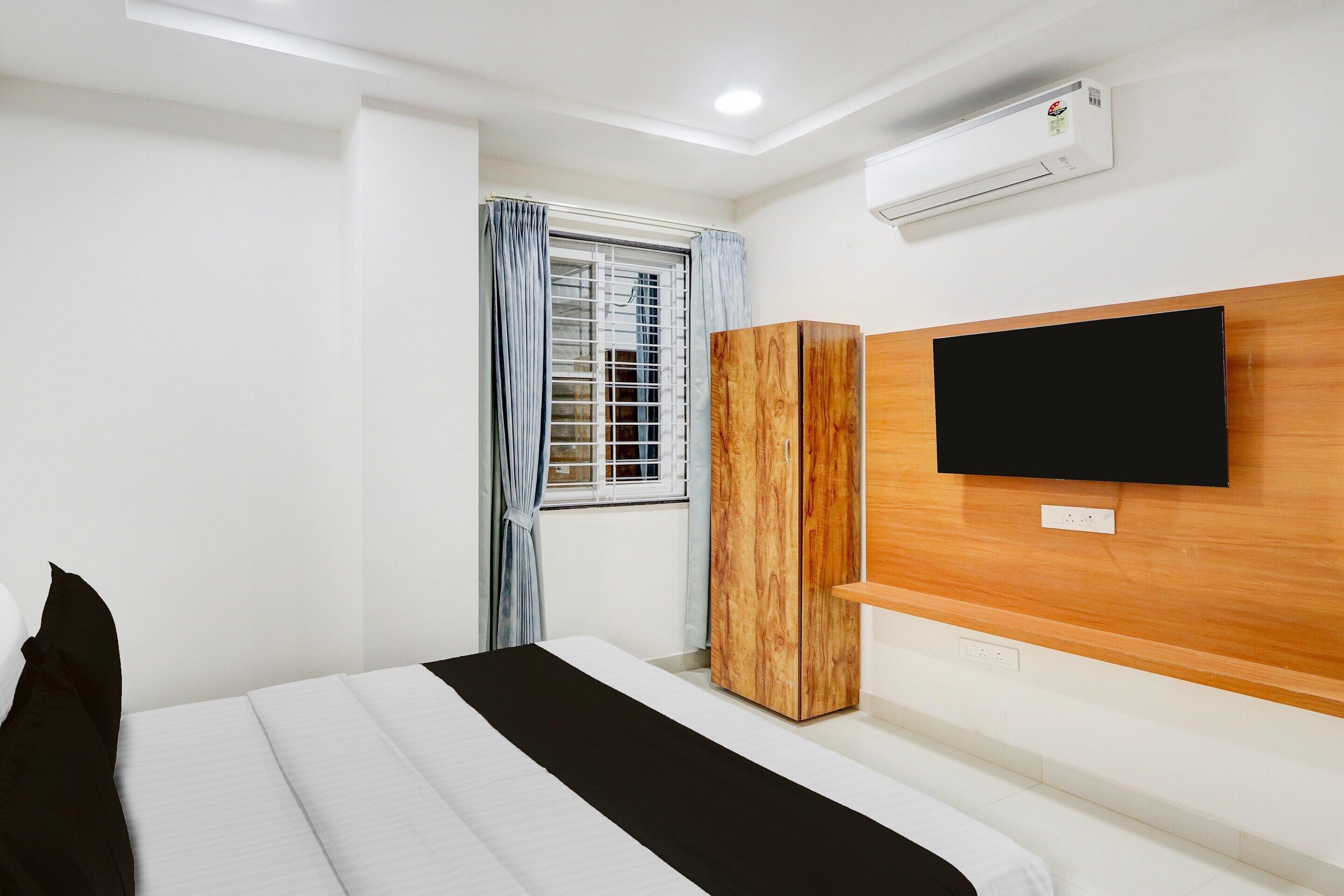 Una habitación de hotel con cama, armario, televisor montado en la pared y aire acondicionado.