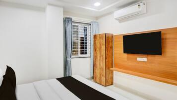 Una habitación de hotel con cama, armario, televisor montado en la pared y aire acondicionado.