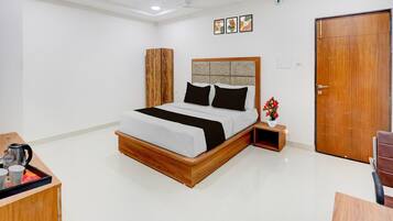 A bedroom with a bed, bedside table, a wooden wardrobe, a door, and a small table with a vase.