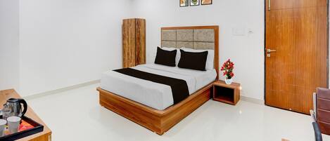A bedroom with a bed, bedside table, a wooden wardrobe, a door, and a small table with a vase.