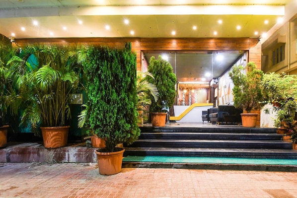 Entrada de hotel con escalones que conducen a una puerta, rodeada de plantas en macetas.