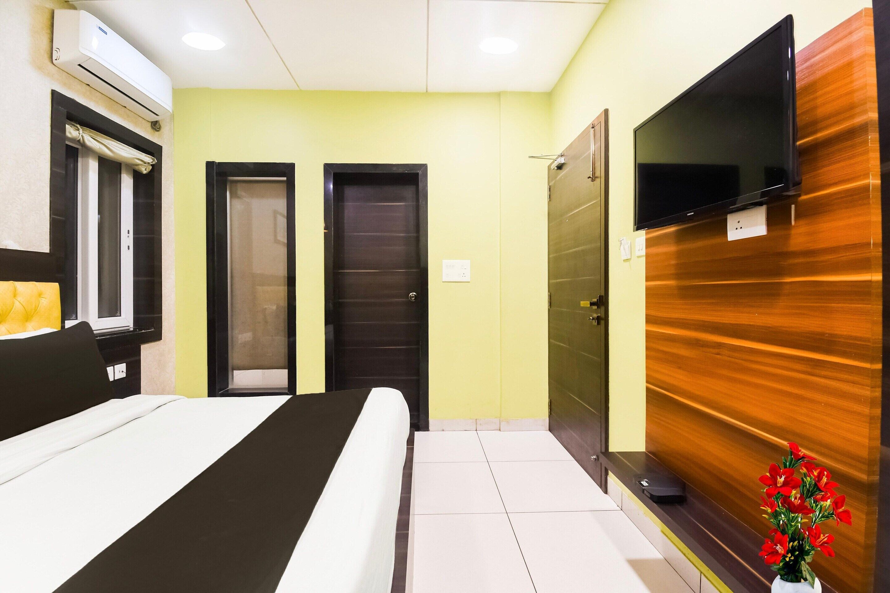 A hotel room with a bed, a television, a door, and an air conditioning unit.