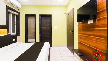 A hotel room with a bed, a television, a door, and an air conditioning unit.