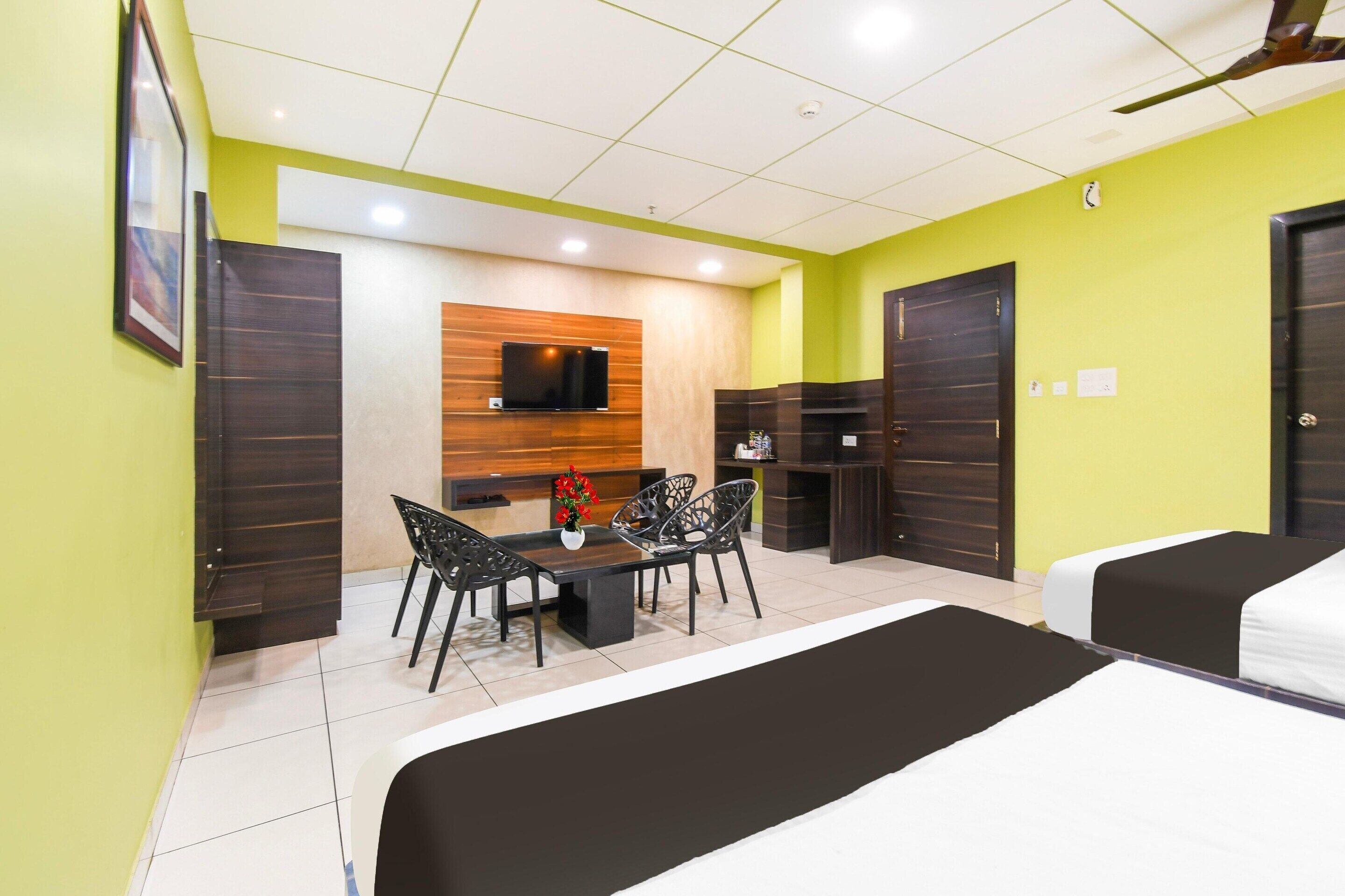 A hotel room with a bed, a desk with a chair, a TV mounted on the wall, and a small table with a vase of flowers.