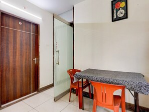 A room with a wooden door, a pull door, a table with a patterned tablecloth, and two orange chairs.