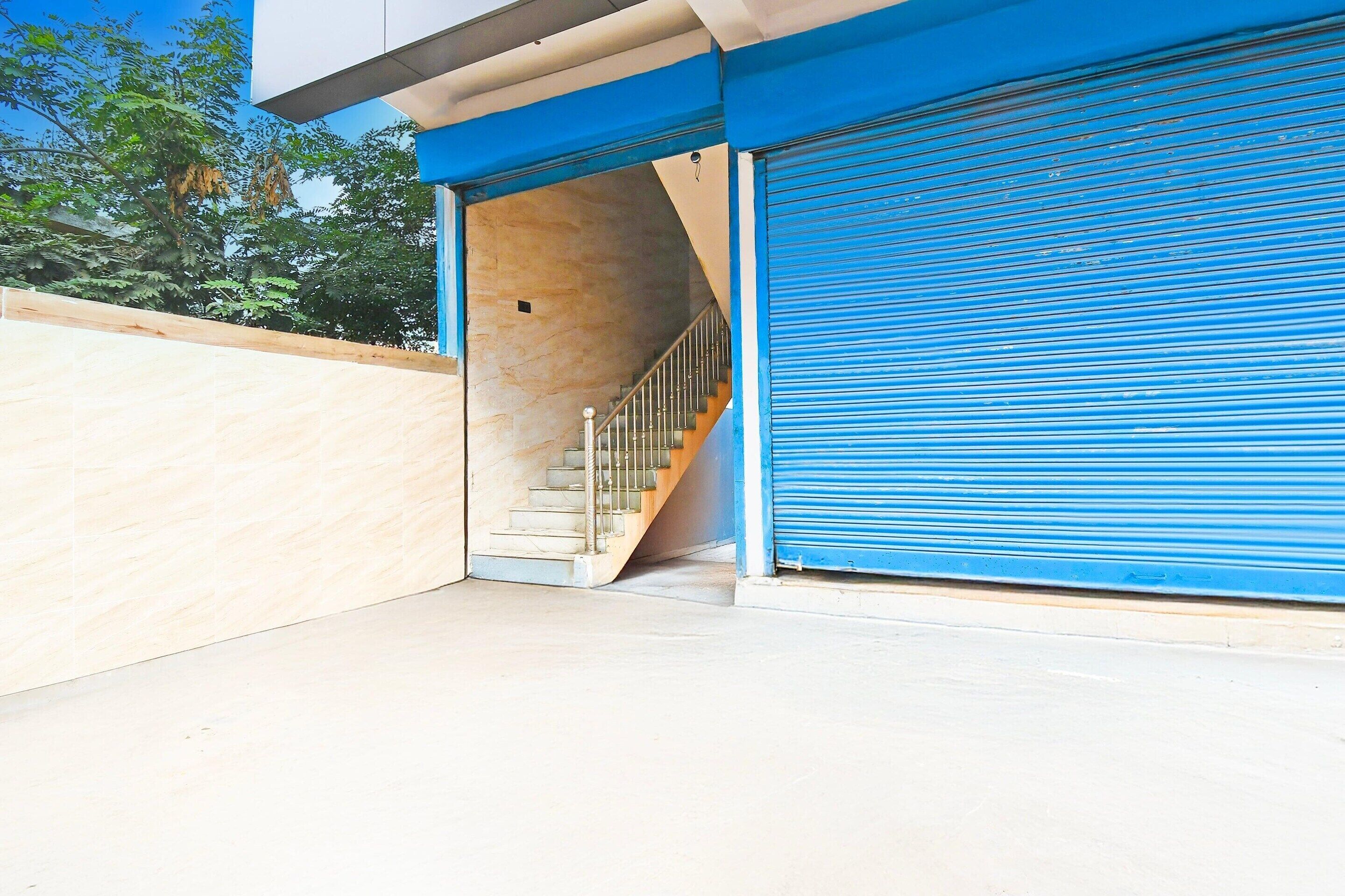 A building entrance with a blue shutter, a staircase leading inside, and a beige wall.