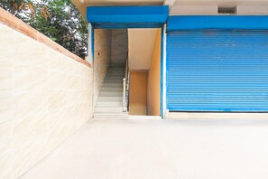 Una entrada de edificio con un persiano azul, una escalera y una pared color beige.