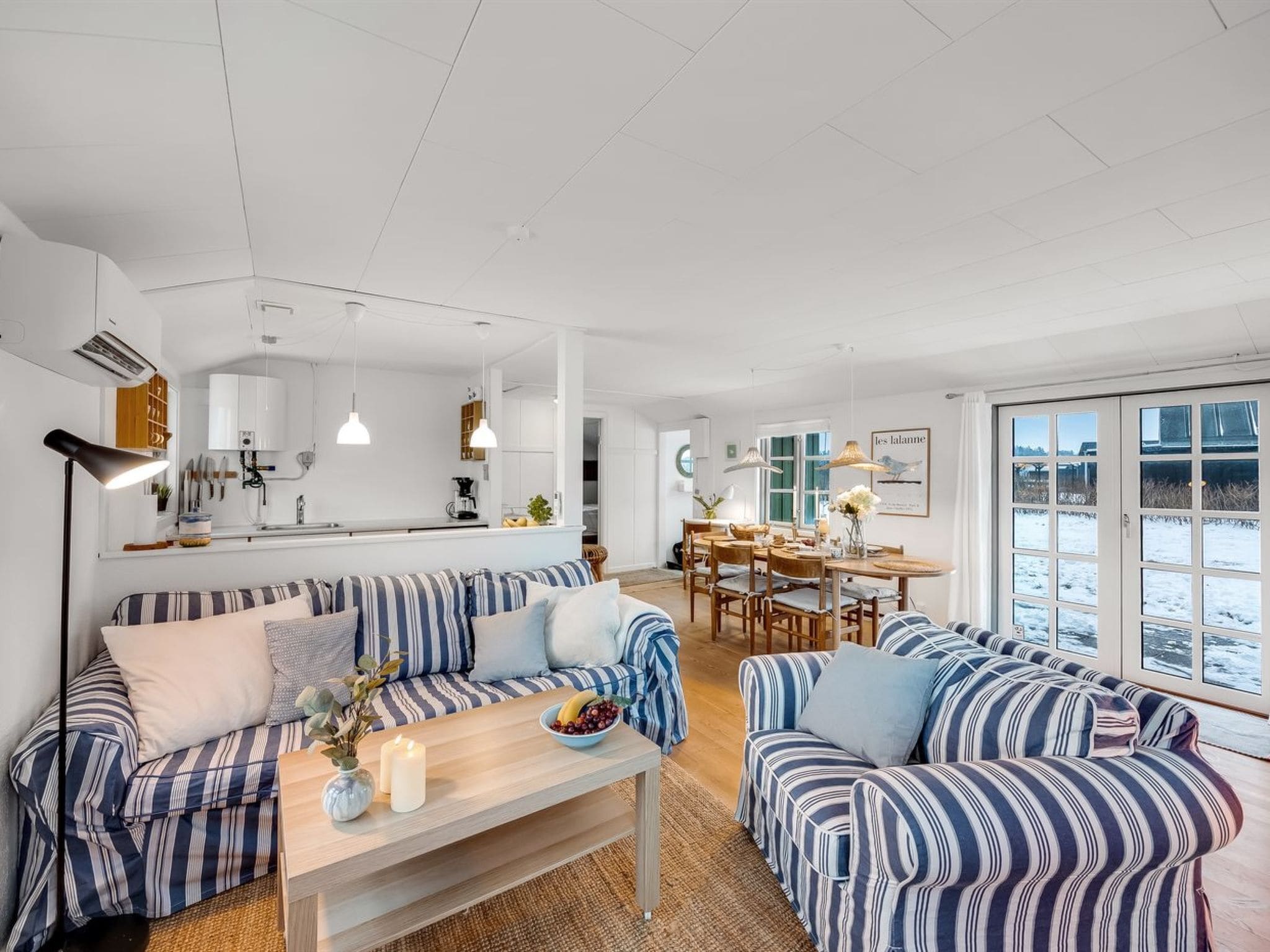Un salon moderne avec des canapés à rayures, une table basse en bois et un coin repas comprenant une table et des chaises blanches.