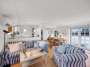 Una sala de estar moderna con sofás a rayas, una mesa de centro de madera y una zona de comedor con una mesa y sillas blancas.