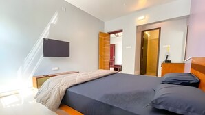 Une chambre à coucher moderne avec un lit, un téléviseur fixé au mur et une armoire avec un miroir.