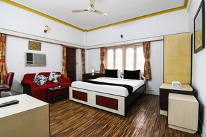 Habitación de hotel con cama, sofá, escritorio, silla, ventilador de techo y ventana con cortinas.