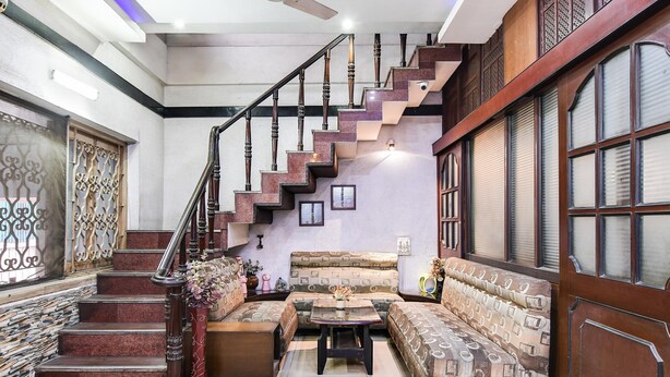 A staircase with ornate railings, a patterned sofa set, and a decorative vase. - Deluxeharry Guest House (Bidhannagar)