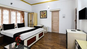 A hotel room with a bed, bedside tables, a TV, a ceiling fan, and a window with curtains. - Deluxeharry Guest House (Bidhannagar)