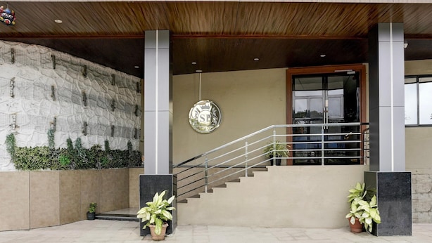 A building entrance with a staircase, a wall-mounted sign, and potted plants.
