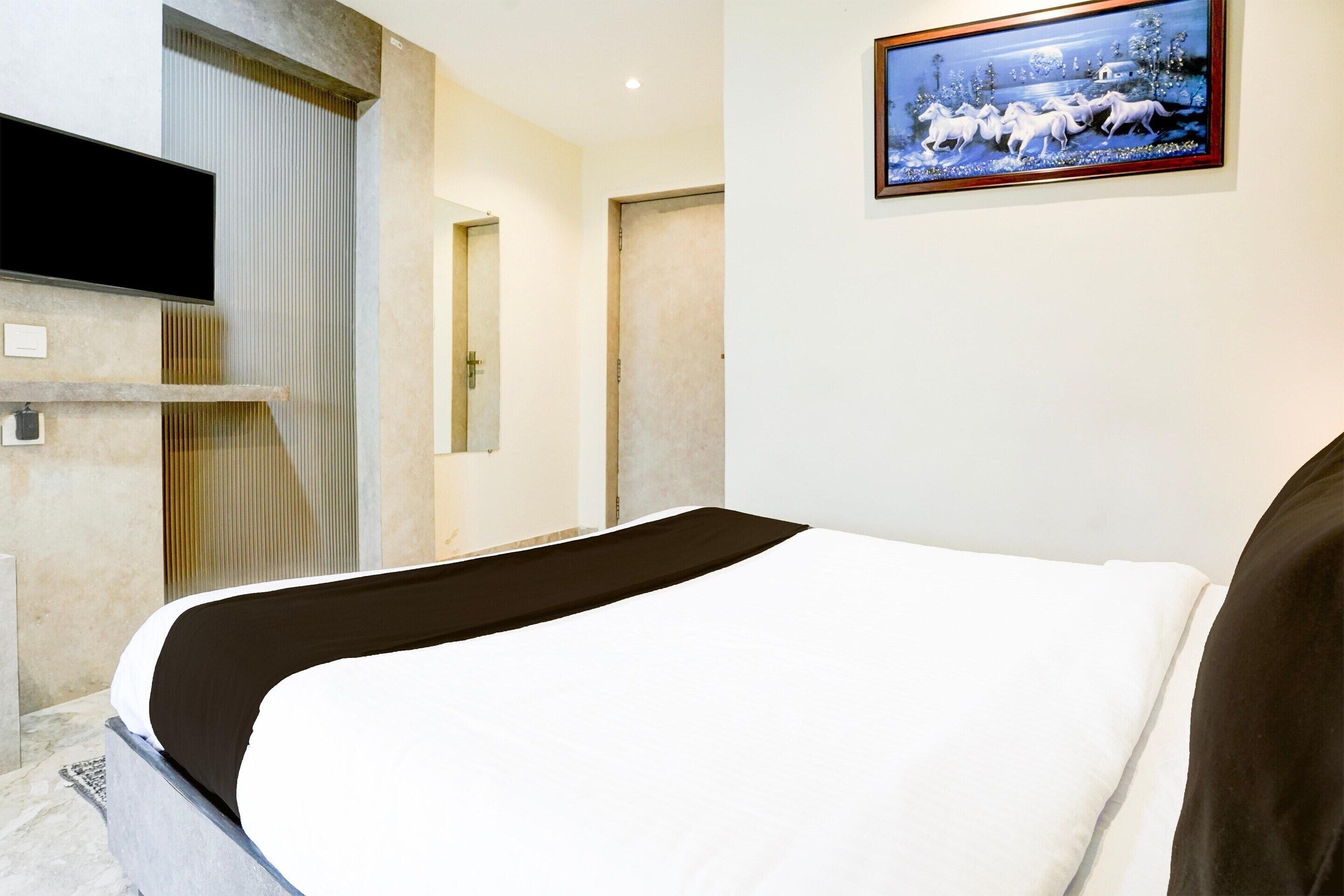 A hotel room with a bed, a TV, a painting, and a door.