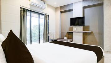 Een hotelkamer met een bed, een aan de muur bevestigde televisie, een raam met gordijnen en een airconditioning.
